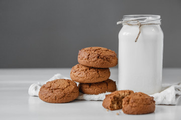 Milk in glass jar and oatmeal cookies near napkin on white table background. Copy, empty space for text