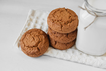 Milk in glass jar and oatmeal cookies near napkin on white table background. Copy, empty space for text