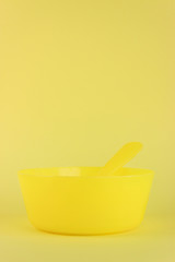 Yellow plastic spoon in yellow plastic empty bowl for kids on yellow background