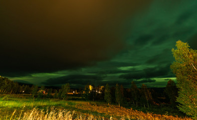 Panoramic photo of strong bright Aurora Borealis behind heavy clouds, meadow and birch trees look very dramatic. Joesjo, Lapland, Northern Sweden. Late summer night.