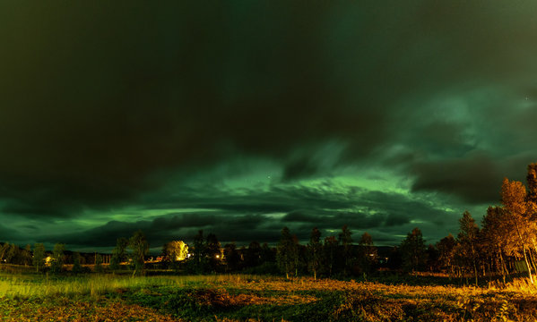 Panoramic photo of strong bright Aurora Borealis behind heavy clouds, meadow and birch trees look very dramatic. Joesjo, Lapland, Northern Sweden. Late summer night.