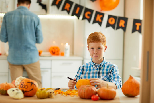 Portrait of little red haired boy carving pumpkin he making Jack O' Lantern for Halloween while sitting at the table at home