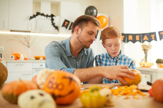 Young father with son sitting at the table and busy with craft they carving pumpkin for Halloween party