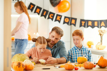 Fototapeta premium Father with his daughter and son sitting at the table with vegetables and making crafts together with mother in the background
