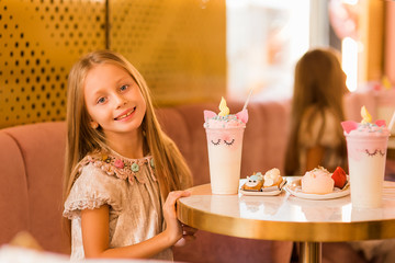 Cute beautiful girl in a cafe eating a cake and a unicorn cocktail.