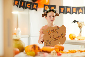 Portrait of cute girl with Hocus Pocus placard looking at camera while visiting Halloween party