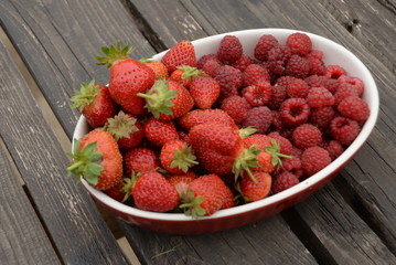 raspberries and strawberries, red berries, in a plate on a dark wooden background