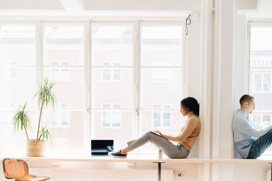 Side view of colleagues working while sitting at desk by window in creative office