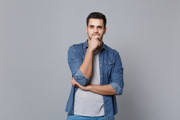 Handsome stylish unshaven young man in denim jeans shirt posing isolated on grey wall background...