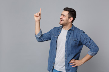 Handsome stylish unshaven young man in denim jeans shirt posing isolated on grey wall background...