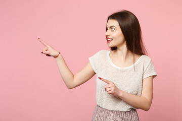 Attractive young woman in casual light clothes posing isolated on pink wall background, studio portrait. People sincere emotions lifestyle concept. Mock up copy space. Pointing index fingers aside.