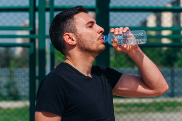 Portrait of a young athlete drinking water on a basketball court on a nice sunny day while wearing a black t-shirt.