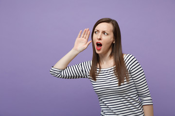 Shocked young woman in striped clothes posing isolated on violet purple background. People...
