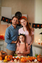 Portrait of young parents standing together with their cute daughter and looking at camera at Halloween party at home