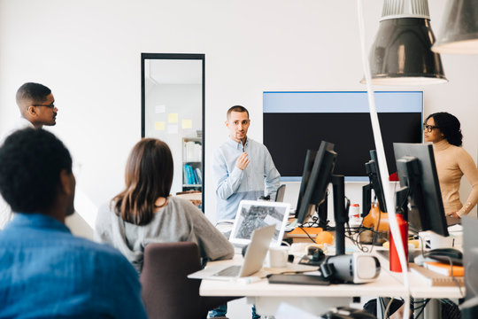 Computer hackers looking at programmer giving presentation during meeting in creative office