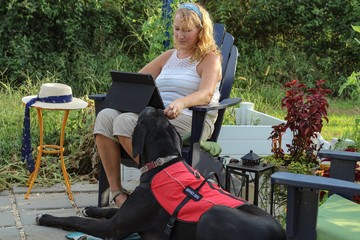 Older adult Caucasian woman with mobility issue is able to enjoy the outdoors on her patio with the help of her loyal and attentive Great Dane service dog by her side