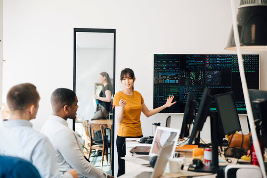 Female hacker interacting with colleagues while giving presentation in office