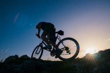 Obraz na płótnie Canvas Silhouette of a mountain biker riding his mountain sportbike on top of a cliff ( hill).