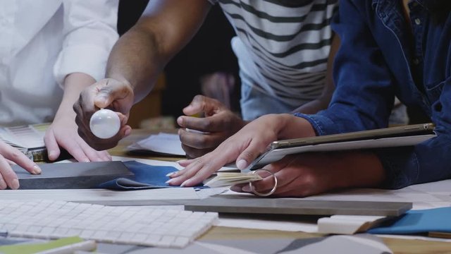 Close-up shot of hands of multiethnic male and female designers working in team on interior project and discussing material and wallpaper samples at meeting