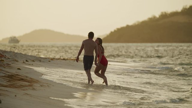 Slow motion of romantic couple holding hands walking on beach and kissing / Petit Tabac, Tobago Cays, St. Vincent and the Grenadines