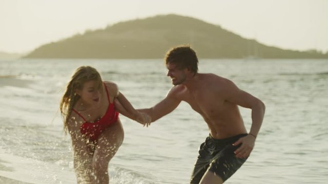 Playful couple splashing each other in ocean then kissing on beach / Petit Tabac, Tobago Cays, St. Vincent and the Grenadines