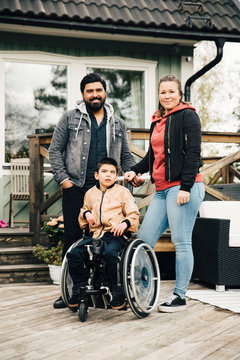 Portrait of smiling parents standing by disabled son sitting on wheelchair against house