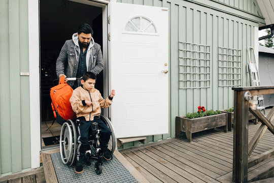 Father with backpack pushing autistic son sitting on wheelchair at doorway