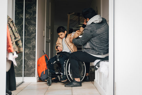Father assisting disabled son in getting dressed at doorway
