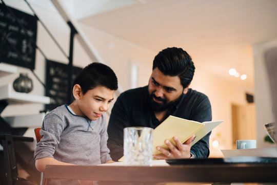 Father teaching autistic son while sitting at table in house