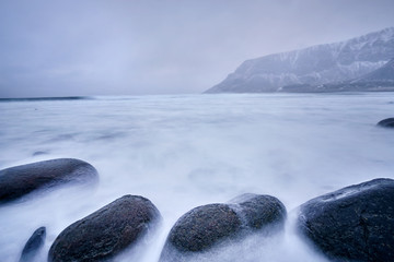 Fototapeta na wymiar Waves of Norwegian sea surging on stone rocks. Long exposure