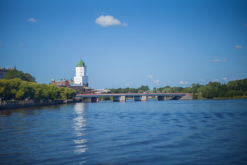 The fable of the medieval Swedish castle in Vyborg against the sky with a cloud and the water of the bay with a bridge.