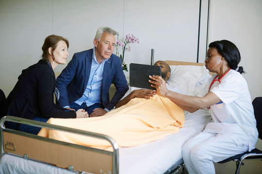 Female medical professional showing medical report on digital tablet to patient and family in hospital