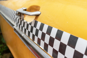 Checkered taxi sign on a yellow taxi car doors close up