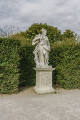 Classic white marble statue of woman with flute in green garden park. Ancient Roman or Greek woman stands on podium. the statue is surrounded by neatly trimmed bushes