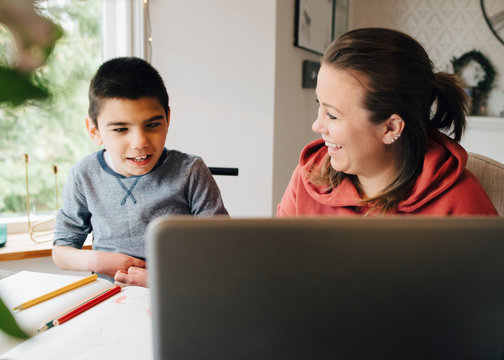 Smiling mother looking at autistic son watching video over laptop while sitting in living room