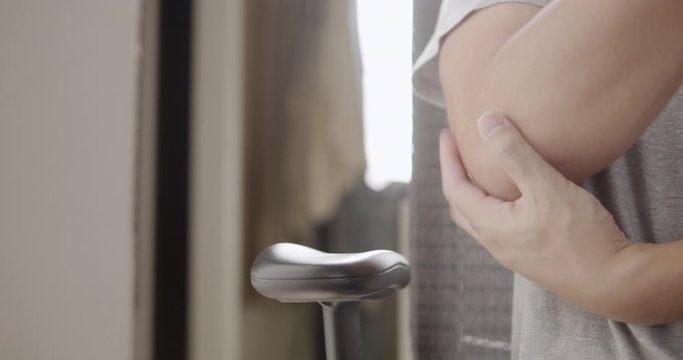Asian man massaging on his elbow pain while sitting on a chair in living room at home.healthcare and medical concepts.