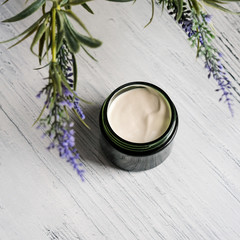 Cosmetic cream container with green herbal leaves on white background