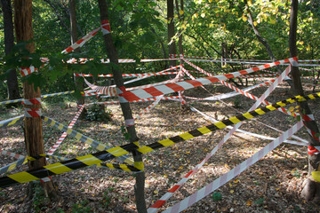 Fototapeta na wymiar Red and white hazard tapes around the incident area in the park, selective focus