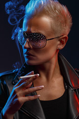 Portrait of a smoking blonde girl with stylish sunglasses on a dark background. Creative color. Studio photography.