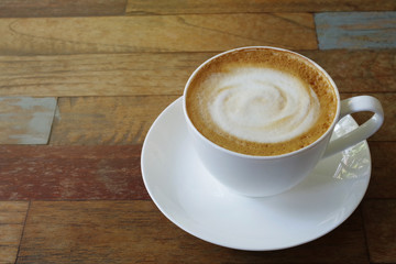 Hot coffee cup cappuccino or latte with stirred spiral milk foam on multicolor plank wood table background in the morning.