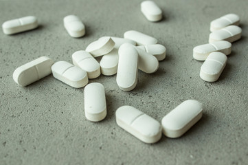 white large oval pills vitamins capsules scattered on a gray concrete background