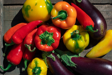 Red, yellow and green bell peppers and eggplant on a wooden background.