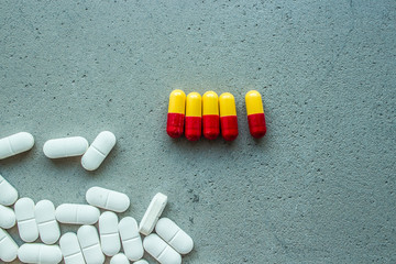 five capsules of vitamin pills red-yellow in color next to white oval capsules on a gray concrete background