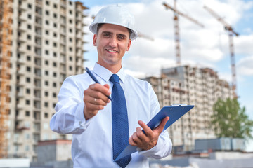 civil engineer in a white helmet makes pencil marks in the documentation.