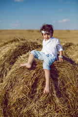 Naklejka na ściany i meble boy child in bandana and white shirt sitting on a bale of hay