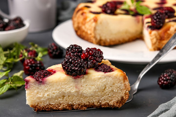 Homemade cottage cheese cake with blackberries with a cut piece of cake located on a dark background, horizontal orientation