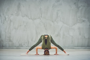 Beautiful slim brunette in red sports wear doing Wide Legged Forward Bend I yoga pose on mat...