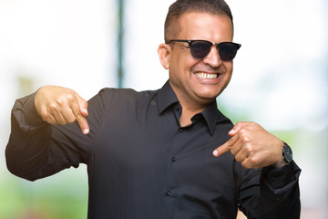 Middle age arab man wearing sunglasses over isolated background looking confident with smile on face, pointing oneself with fingers proud and happy.