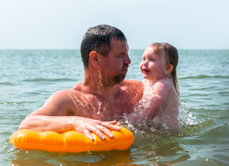 A father swims with his dauter. It's her first time swimming.