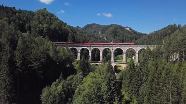 Aerial view of red train rides on famous Kalte Rinne Viaduct on historical Semmering mountain railway (Semmeringbahn), Lower Austria.